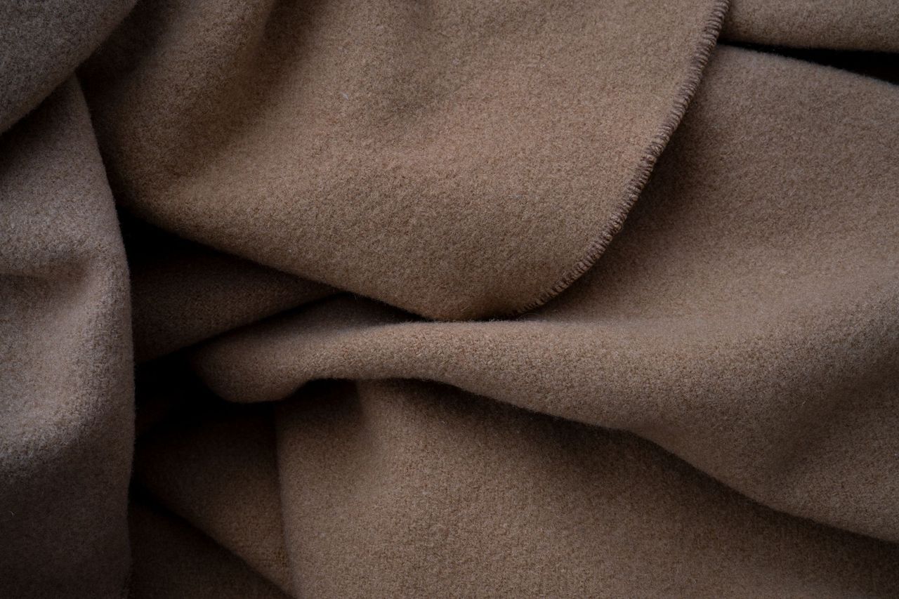 Folded cashmere jumpers in cream, camel and grey on a linen surface