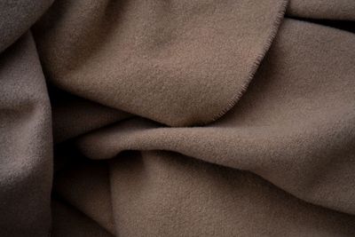Folded cashmere jumpers in cream, camel and grey on a linen surface