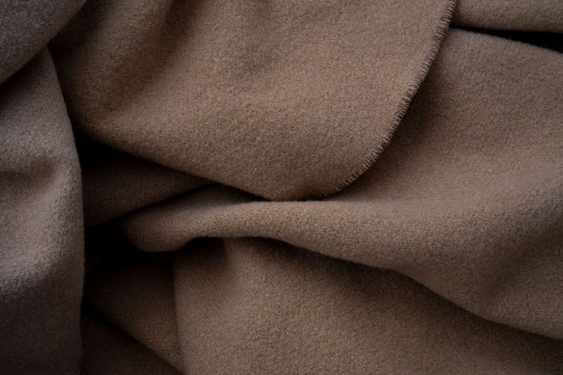 Folded cashmere jumpers in cream, camel and grey on a linen surface